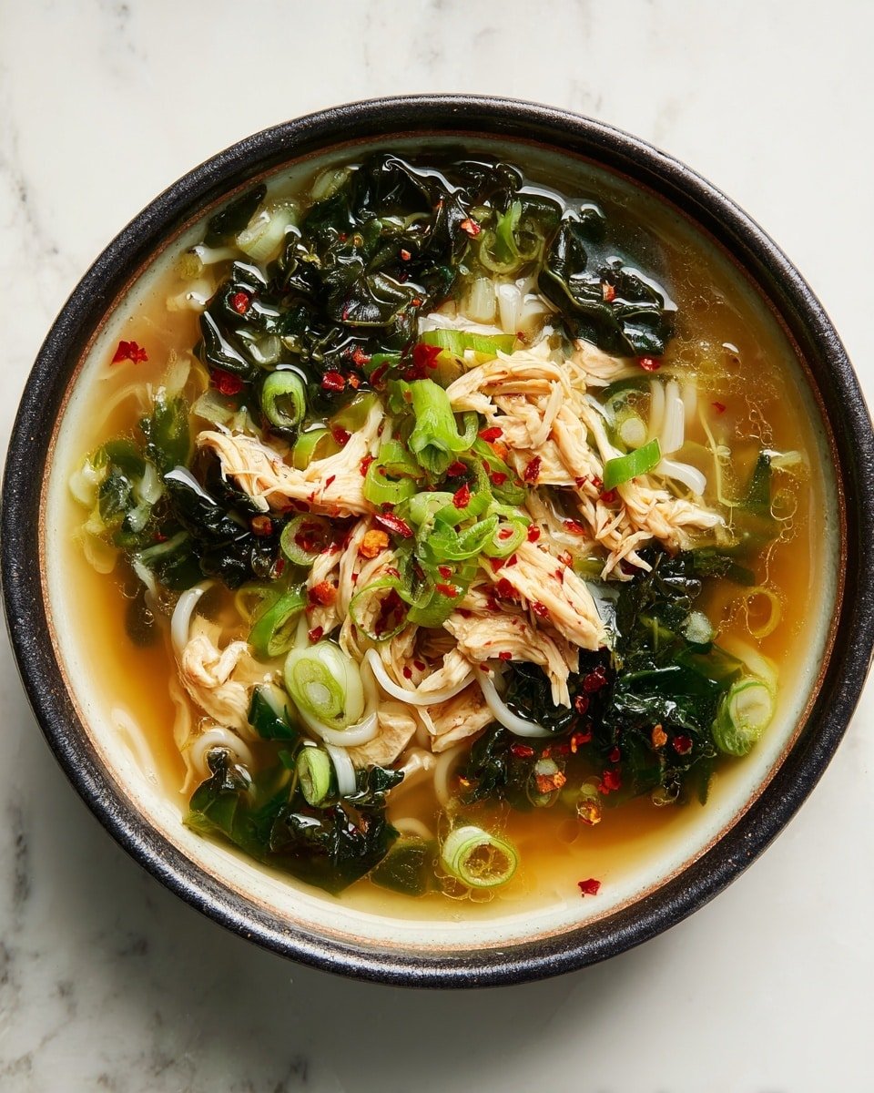 A round white bowl with a dark rim holds a clear broth soup filled with three main layers: thin white noodles at the bottom, shredded light beige chicken pieces in the middle, and dark green leafy vegetables floating on top. The soup is garnished with sliced light green scallions and scattered red chili flakes, adding color contrast. The liquid reflects light, making the broth look warm and fresh. The bowl is set against a white marbled surface. Photo taken with an iphone --ar 4:5 --v 7 — Ginger Garlic Chicken Noodle Soup, healthy chicken noodle soup, quick comforting chicken soup, flavorful chicken broth recipes, cozy noodle soup