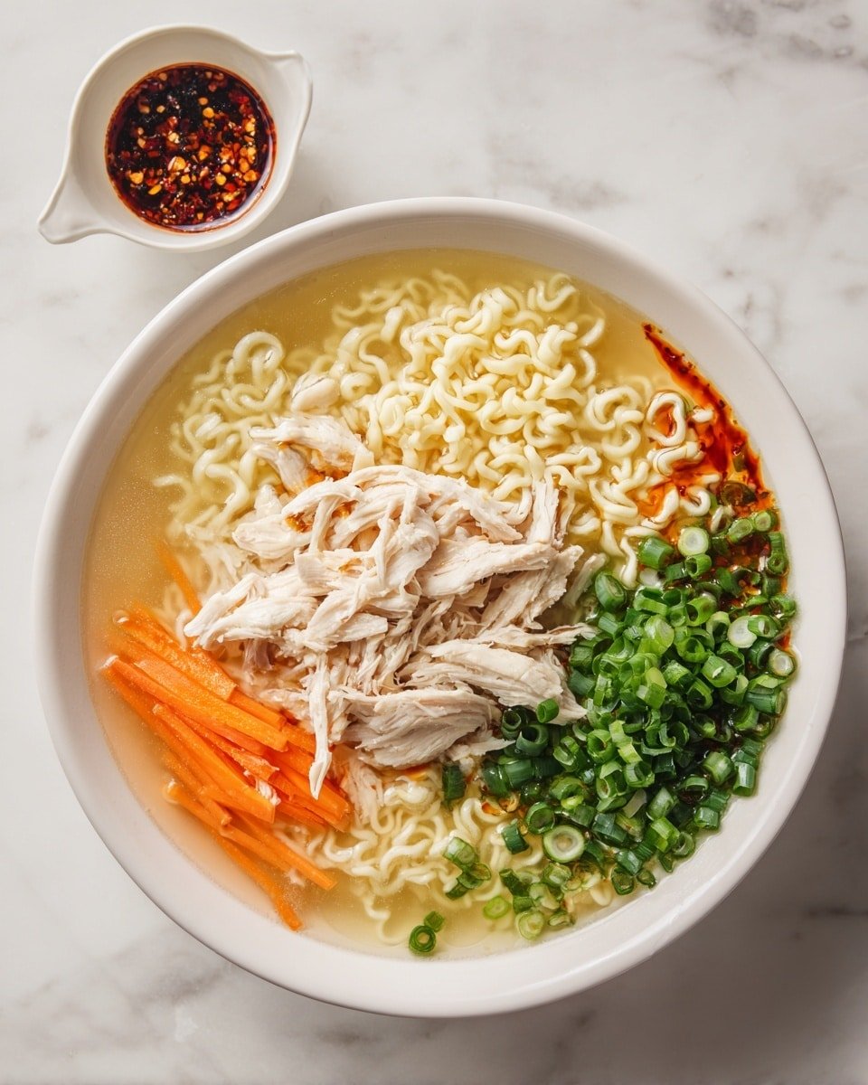 A white bowl filled with clear broth soup, layered with light yellow curly noodles on the top right, shredded white chicken pieces on the bottom left, thin bright orange carrot sticks in the middle, and a thick pile of chopped green onions on the right. There are reddish chili oil spots drizzled over the soup, giving a spicy look. To the top left of the bowl, there is a small white cup holding a dark red sauce with chili flakes. The entire scene is set on a white marbled surface. photo taken with an iphone --ar 4:5 --v 7 — Aromatic Ginger Scallion Chicken Noodle Soup, chicken noodle soup with ginger and scallions, comforting chicken soup with ginger and scallions, healthy ginger scallion chicken soup, easy homemade chicken noodle soup