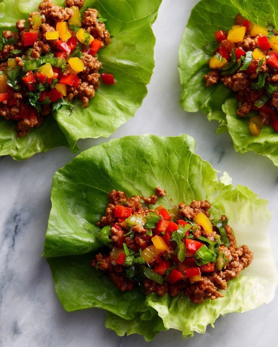 Three lettuce wraps lie on a white marbled surface. Each wrap has one large, green ruffle-edged leaf as the base, holding a middle layer of brown cooked ground meat and topped with a mix of bright red, yellow, and green chopped bell peppers. The texture of the lettuce is crisp and fresh, while the meat appears juicy and crumbly. The colorful peppers add a fresh and vibrant look on top. Photo taken with an iphone --ar 4:5 --v 7 — Keto Beef Tacos, low-carb beef tacos, keto taco recipes, gluten-free beef tacos, keto dinner ideas